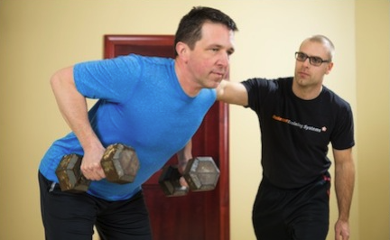 Trainer works with man doing standing dumbbell rows